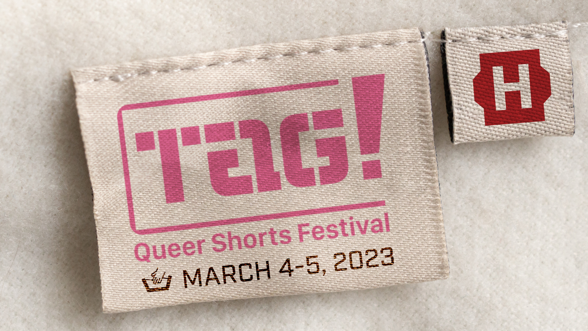 Clothing tag with the logo of the Tag Queer Shorts festival next to a second label with the Hollywood Theatre logo.